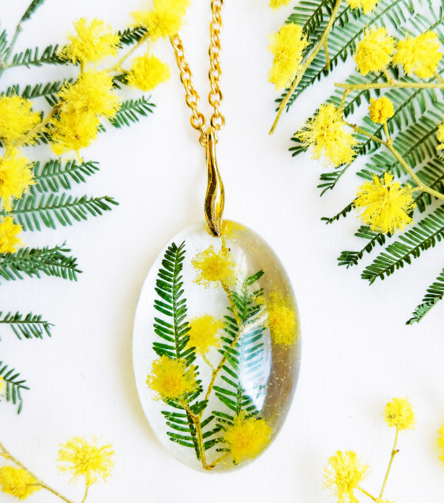 Gold chain necklace with an oval resin pendant containing pressed yellow mimosa flowers and fern leaves