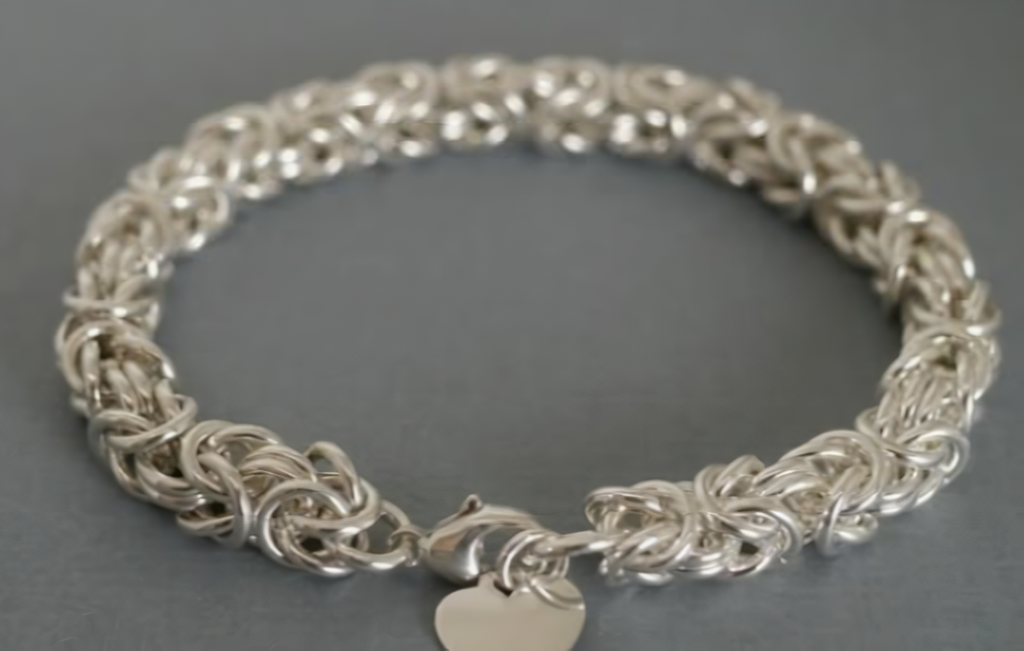 Silver woven chain bracelet with a heart-shaped charm on a gray surface