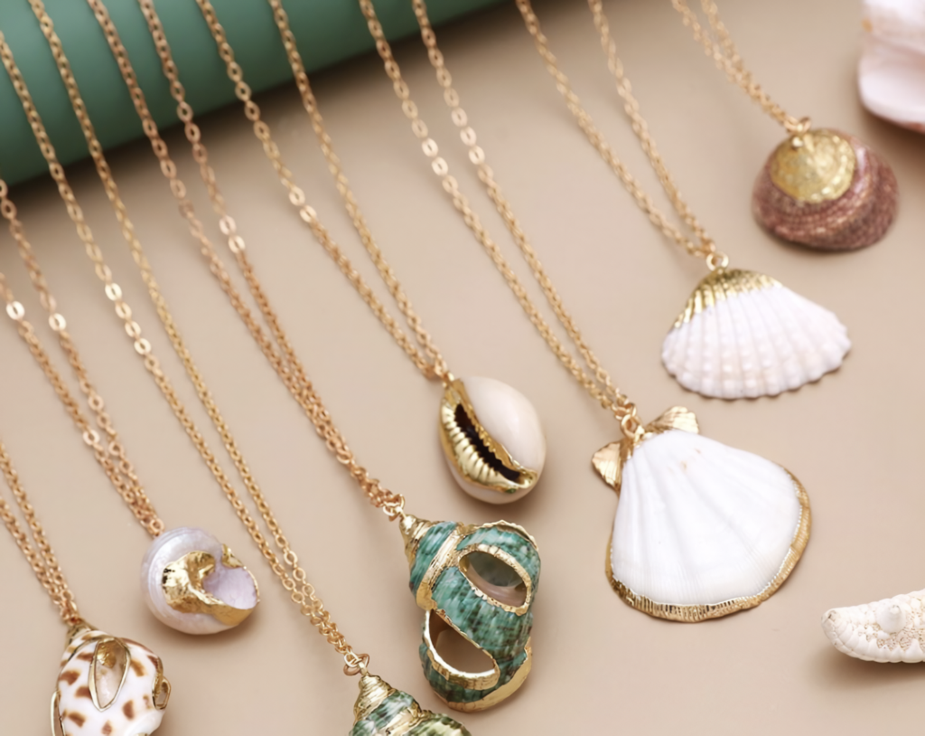 Gold-tone chain necklaces with assorted shell pendants laid on a beige surface.