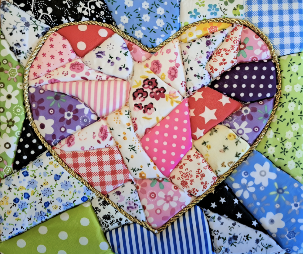 Heart-shaped patchwork quilt made of colorful floral and geometric fabric patches with a gold trim edge.